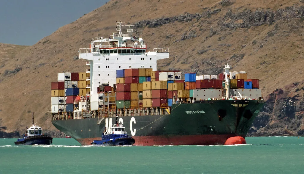 A loaded container ship under tug escort entering port